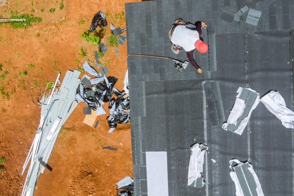 Air nail gun is used by roofing contractor to install new asphalt bitumen shingles on roof of house