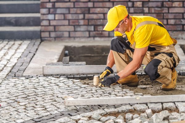 A skilled worker carefully installs cobblestones on a walkway, focused on precision at a construction site under daylight conditions, showcasing craftsmanship.